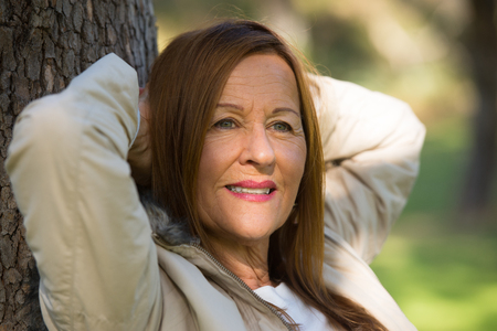 Portrait attractive mature woman with long hair posing happy relaxed, thoughtful and confident outdoors in park, friendly smiling.の写真素材