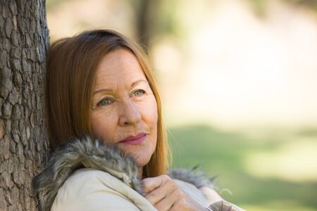 Portrait attractive beautiful mature woman sitting happy relaxed, with contemplating smile outdoors, blurred background.の写真素材
