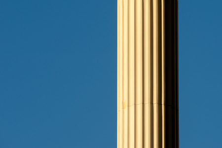 Partly visible sunlit marble column against the background of clear blue sky. Free space to enter...