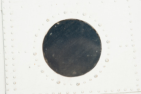 Closeup view of a fuselage area of a vintage aircraft. The area is covered with rivets and painted white. Dusty round viewport or illuminator in the middleの写真素材