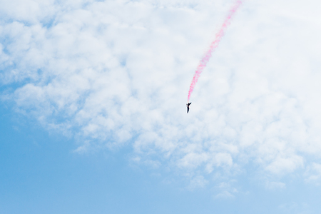 Training jet plane aerobatics in the vastness of the blue sky and white clouds. Red color trace behind the aircraft. Free space to enter text.の写真素材