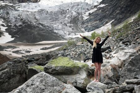 happy young blond woman in black dress among the huge stones on the glacier. Mestia, Georgiaの写真素材
