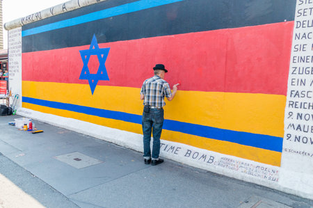 Berlin, Germany - August 16, 2018: Man painting german flag on Berlin Wall.のeditorial素材