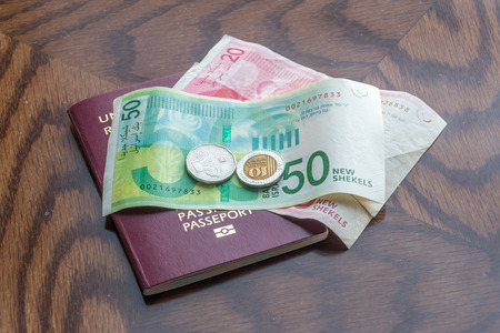 Passport with Israeli new shekel banknotes and coins on wooden table.の写真素材