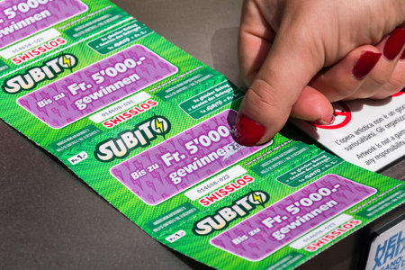 Lugano, Switzerland - June 1, 2019: Woman hand scratching a Switzerland SWISSLOS lottery scratch card with nail.のeditorial素材