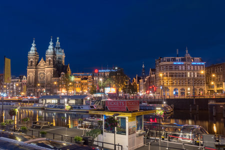 Amsterdam, Netherlands - June 6, 2019: Canal and buildings over canal with The Basilica of Saint Nicholas at night.のeditorial素材