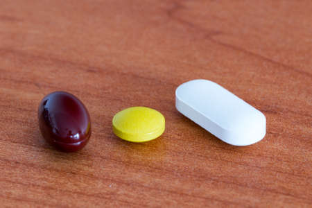 Brown capsule, yellow and white pills on wooden table.の写真素材
