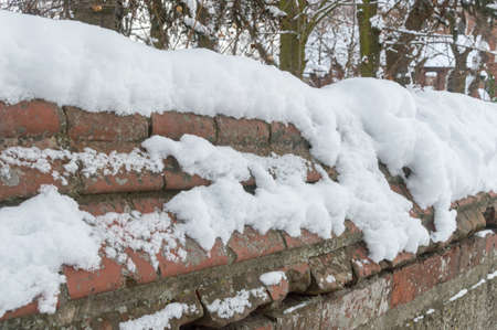 Old brick fence in winter covered with snow.の写真素材
