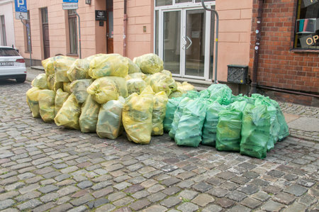 Torun, Poland - July 26, 2021: Plastic bags with segregated garbage on the street. Yellow plastic bags and green ones with glass.のeditorial素材