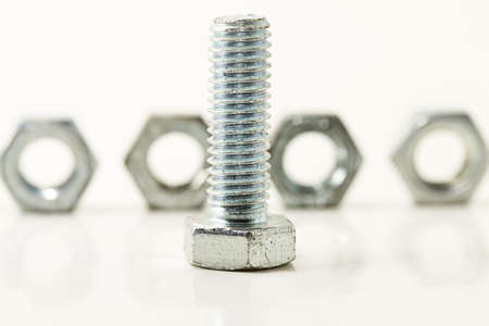 one screw standing in front of four bolts on white backgroundの写真素材