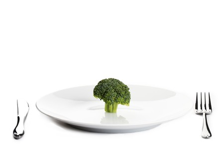 one green broccoli on a plate with knife and forkの写真素材