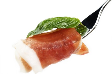 smoked bacon with basil on a fork in front of white backgroundの写真素材