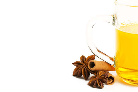 half glass with yellow tea, two cinnamon sticks and two star anise on white backgroundの写真素材