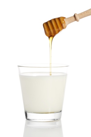 honey falling from a honey dipper in a glass of milk on white backgroundの写真素材