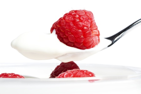 closeup of a raspberry on a spoon with yogurt over a dessert with raspberries on white backgroundの写真素材