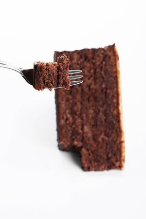 piece of a chocolate cake on a fork over a chocolate cake on white backgroundの写真素材