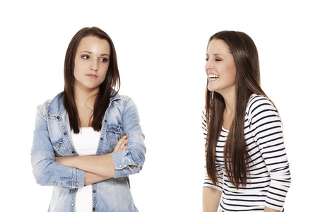 teenager laughing at her upset sister on white backgroundの写真素材