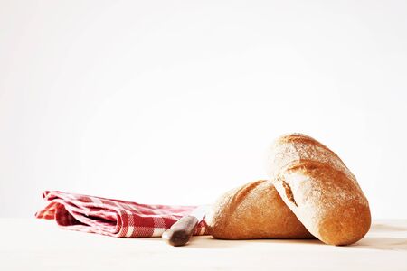 two wholemeal buns with a towel and a old bread knife in natural lightの写真素材