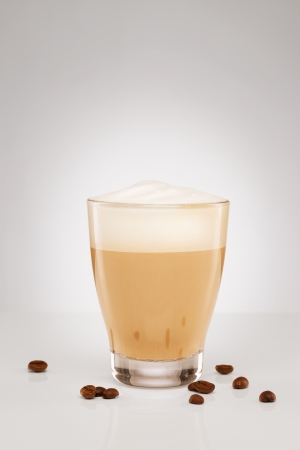cappuccino with milk foam in a small glass with coffee beans on grey backgroundの写真素材