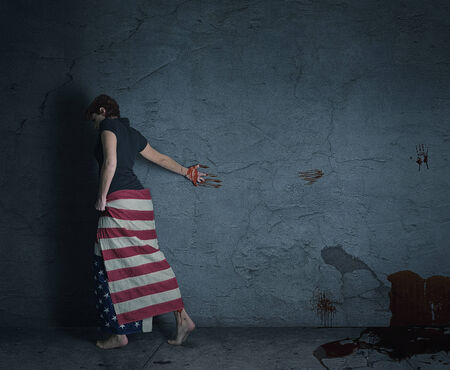 young woman at a grey wall wearing american flag with a blood trail behind herの写真素材