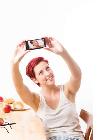 blonde happy woman at breakfast making a self portrait with her smartphone on white backgroundの写真素材