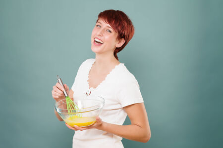 happy redhead woman stirring eggs in a glass bowlの写真素材