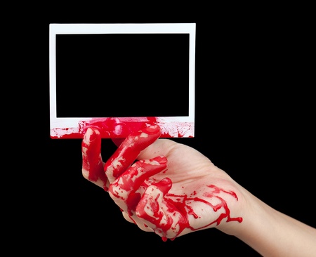 A blood covered hand holding up a piece of blank instant film isolated on black.の写真素材