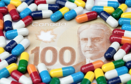Hundred dollar Canadian bill covered with colorful pills on a white background.の写真素材