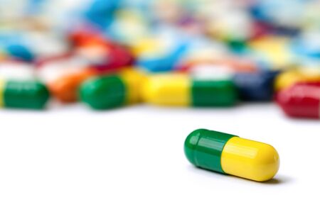 A macro closeup shot of a green and yellow pill with many pills in a blurred background isolated on white.の写真素材