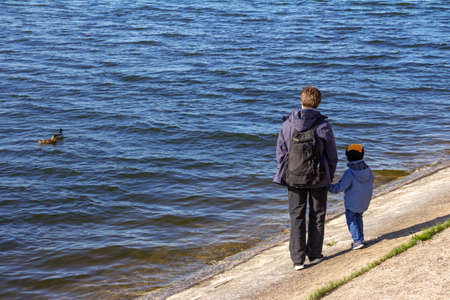 Father and little son are walking along the lake on a sunny day. Horizontal view. High quality photoの写真素材