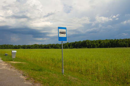 Bus stop sign on a background of blue cloudy sky, green field and forest on a summer sunny day. High quality photoの写真素材
