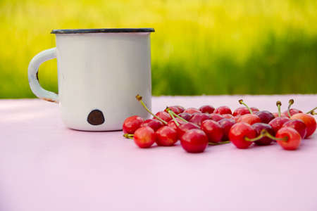 White vintage White metal vintage shabby mug with cherry berries on blurred light green background. High quality photoの写真素材