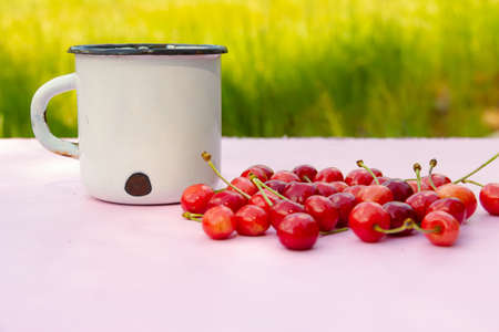White vintage White metal vintage shabby mug with cherry berries on blurred light green background. High quality photoの写真素材