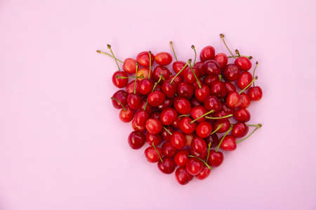 Red sweet cherries in heart shaped layout on light pink background. High quality photoの写真素材