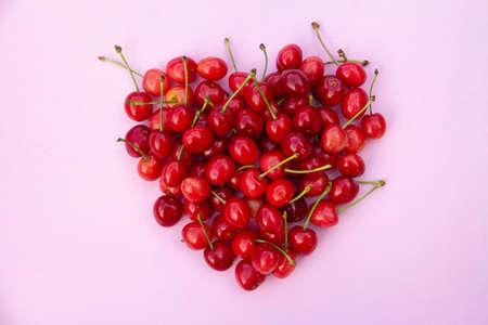 Red sweet cherries in heart shaped layout on light pink background. High quality photoの写真素材
