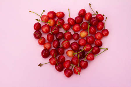 Red sweet cherries in heart shaped layout on light pink background. High quality photoの写真素材