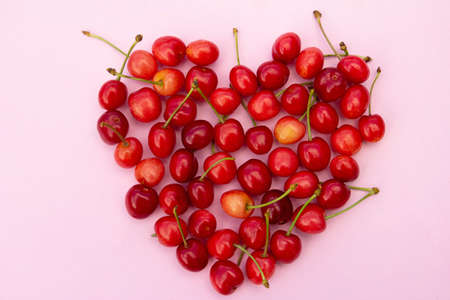 Red sweet cherries in heart shaped layout on light pink background. High quality photoの写真素材
