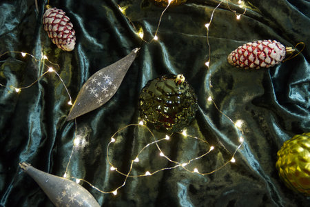 Christmas tree toys and light garland lying on dark green velvet background. Christmas decorations close up photo.の写真素材