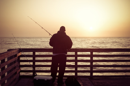 Man Fishing in the ocean from a pier in early morning.の写真素材
