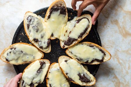 Molletes. Vegetarian Mexican food similar to bruschetta. Refried beans and melted cheese on toasted bread. White and brown skinned hands choosing food itemsの写真素材
