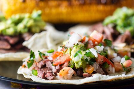 Mexican carne asada tacos, literally grilled meat tacos. These are chopped barbecued beef served on soft corn totillas with salsa verde and pico de galloの写真素材