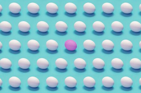Single colored egg among white eggs solid color background