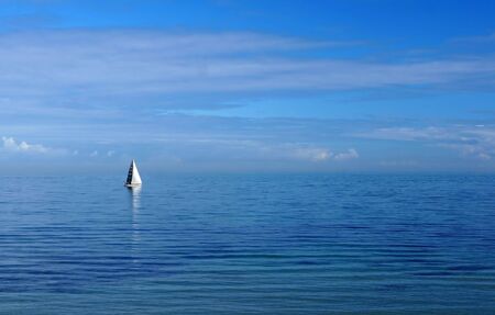 Blue on Blue - single white-sailed yacht on a pastel-blue seaの写真素材