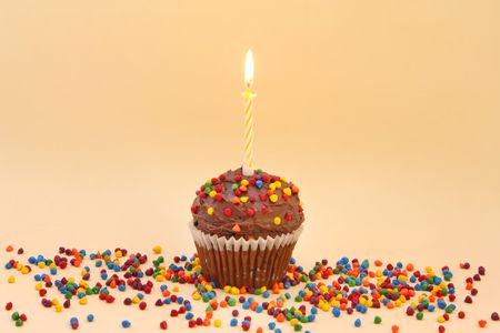 Chocolate frosted cupcake with single candle, and colourful sprinkles.の写真素材