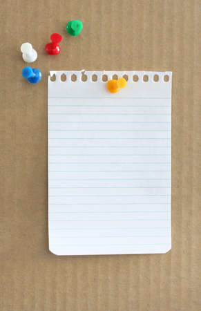 Blank torn notepaper on a noticeboard, with push pins.の写真素材