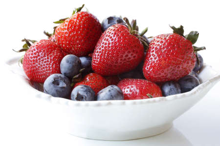 Strawberries and blueberries fill a small white bowl.  Luscious fresh berry fruit.の写真素材