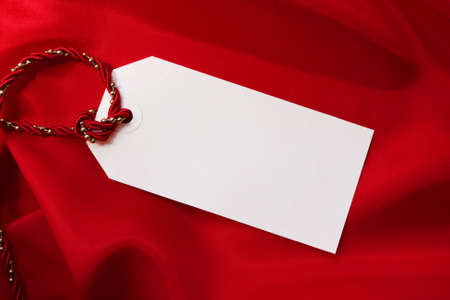 Blank gift tag on folds of red satin, tied with red and gold festive cord.の写真素材