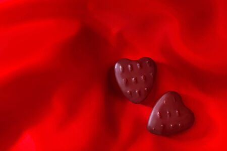 Two heart-shaped chocolates on red satin background.  Be my Valentine!の写真素材
