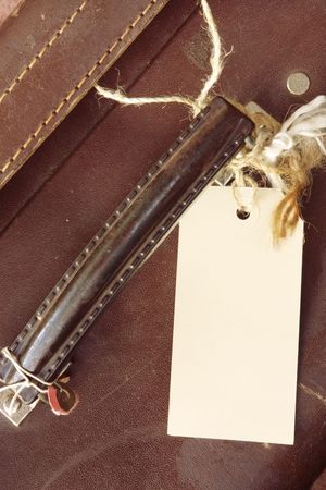 Blank luggage label tied to handle of battered brown leather suitcase.  Close-up view.の写真素材