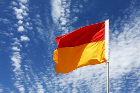 A red and yellow swimming safety flag on an Australian beach, against vibrant blue sky with...